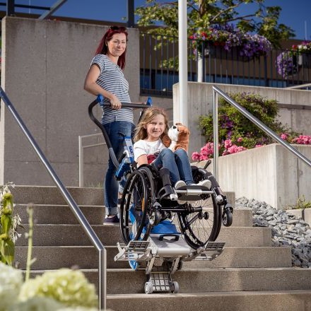 Mother helping her daughter in a wheelchair down several stairs.